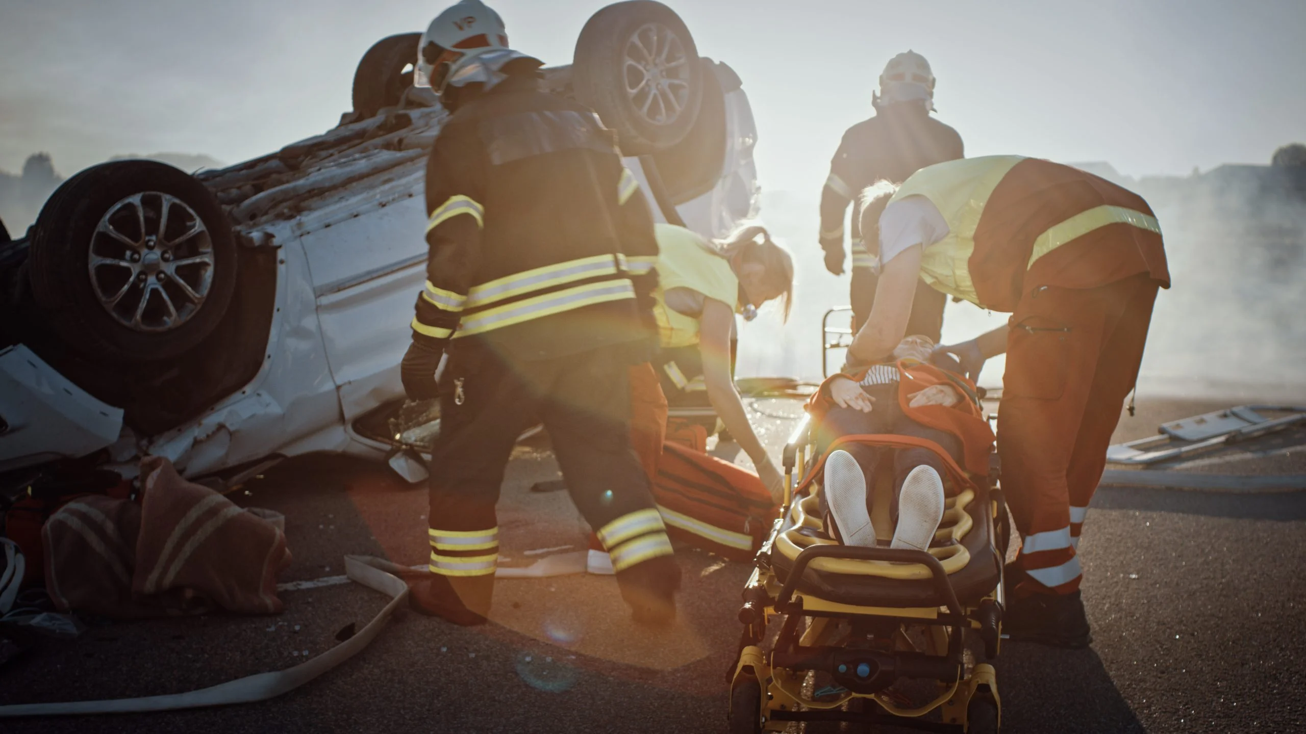 On the car crash traffic accident scene: rescue team of firefighters pull female victim out of rollover vehicle, they use stretchers carefully, hand her over to paramedics who perform first aid